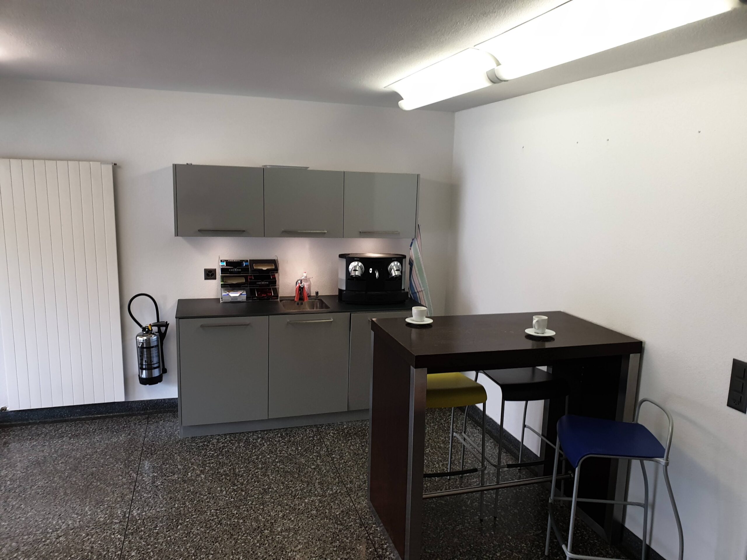 kleine Küchenzeile mit Kaffeemaschine und einem Tisch mit Barhockern