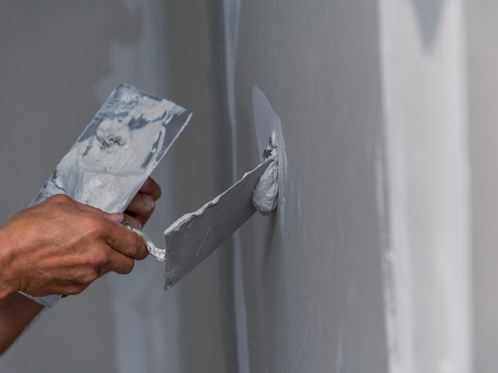 Zwei Hände sind ersichtlich, welche Spachtel halten und die Wand spachteln.